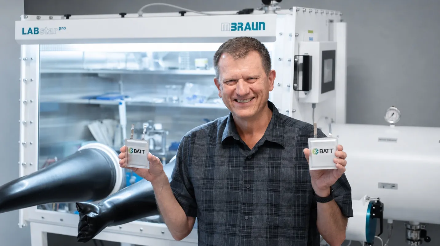 X-BATT founder holding pouch cells in front of an mBRAUN LABstar Pro glovebox